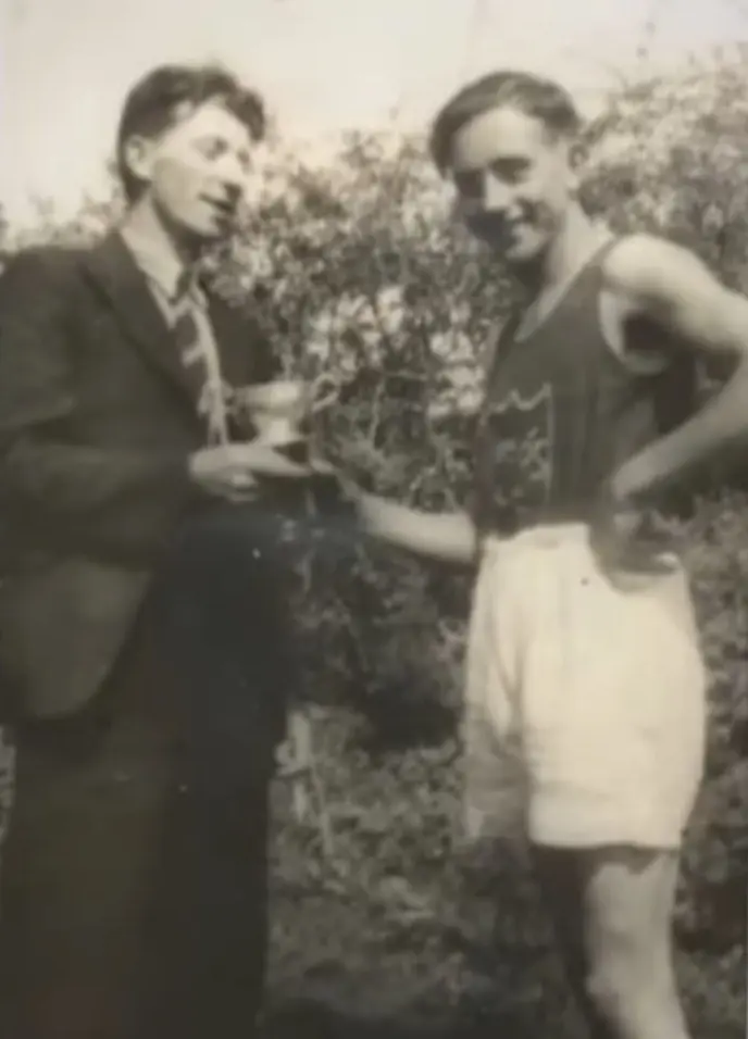 A man in a suit presenting a cup to a man in athletics kit